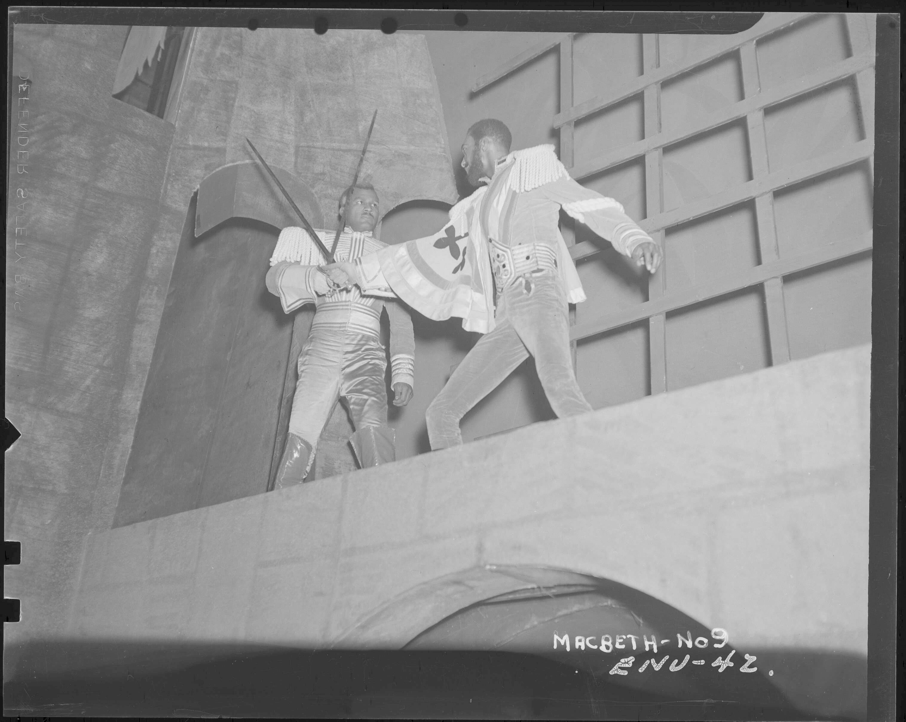 Photograph of Charles Collins (left, Macduff) and Maurice Ellis (right, Macbeth) swordfighting atop a plinth during the climax of the play.